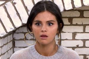 Selena Gomez with surprised expression, wearing large hoop earrings, and a grey sweater