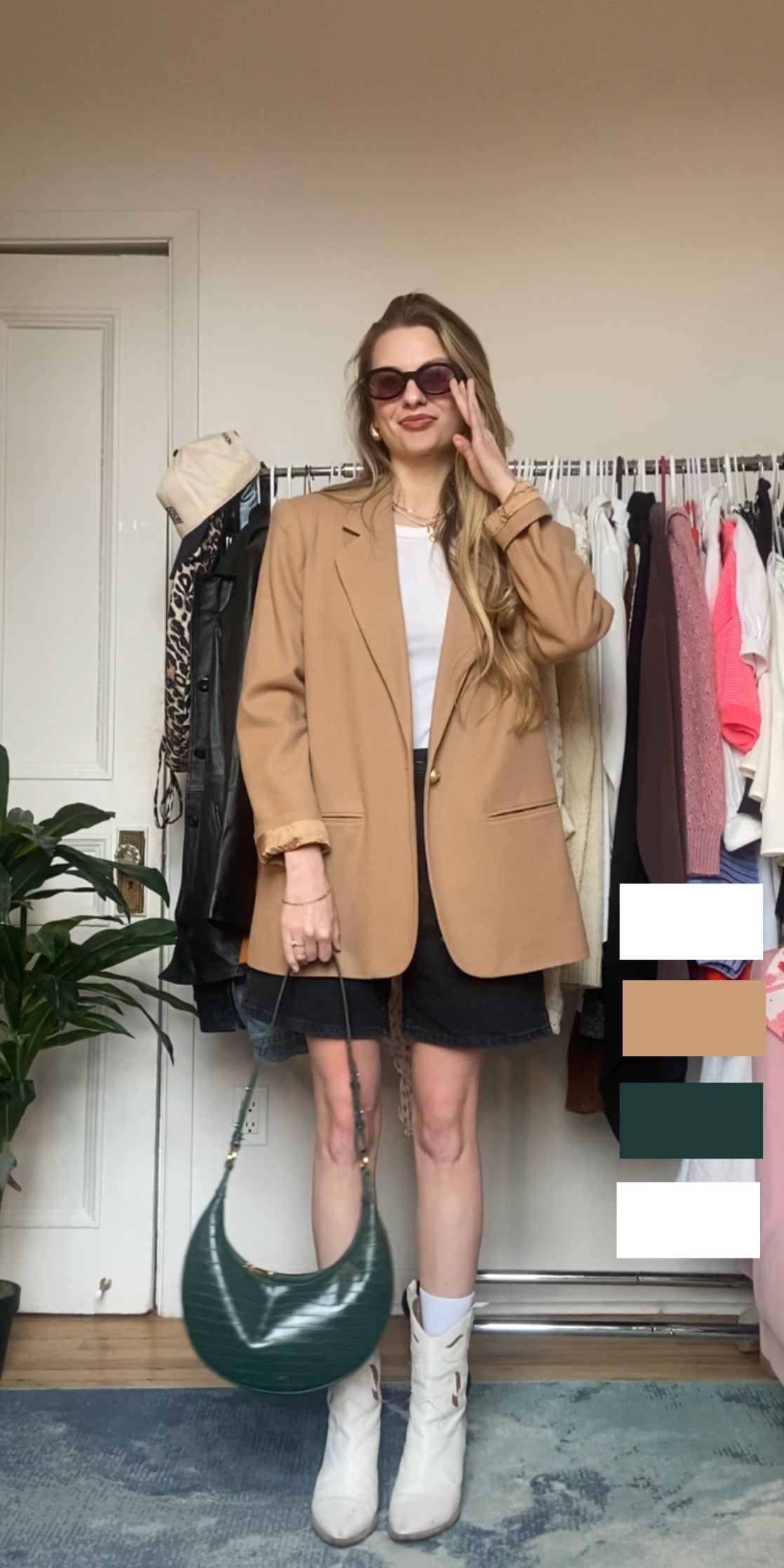 Woman in oversized blazer, mini skirt, and boots, holding purse, standing in a room with clothes rack