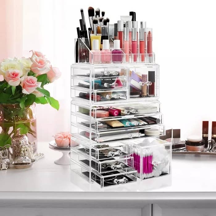 Clear acrylic makeup organizer with drawers and compartments, filled with various cosmetic items