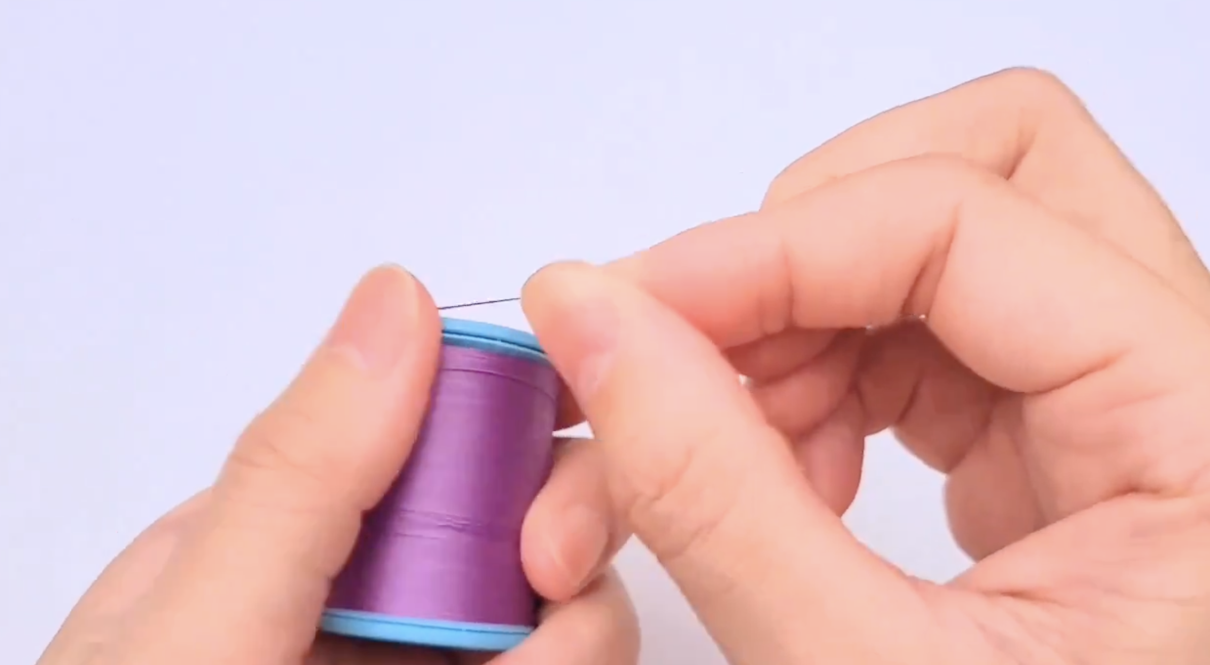手が青色の糸のスプールを持っています。
