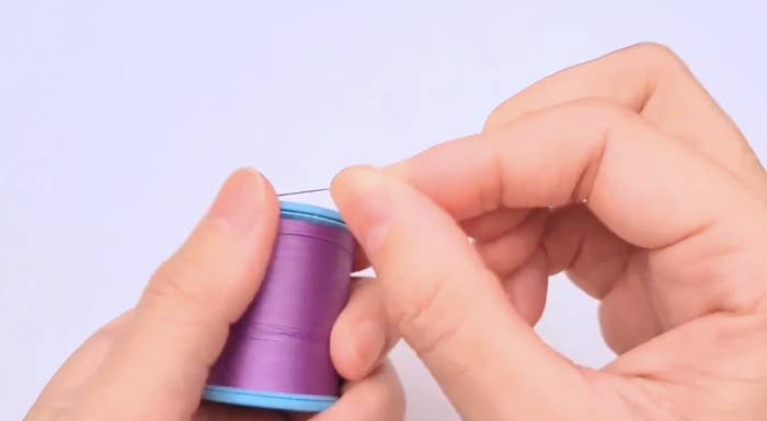 手が青色の糸のスプールを持っています。
