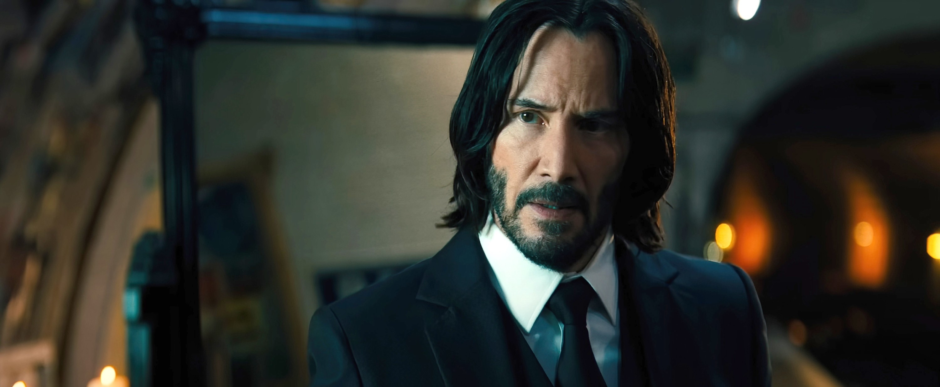 Keanu Reeves wearing a classic black suit and tie in a movie scene