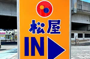 Sign with Japanese characters, "IN" arrow and logo, indicating entrance and parking availability