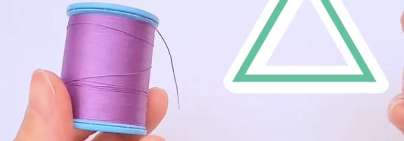 手が紫の糸の巻き取られたボビンを持っており、右側に緑色の三角形のシンボルがある。
