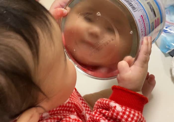 赤ちゃんが鏡を見ている。鏡にはテキストがあるが、読めない。服は赤白チェック柄です。