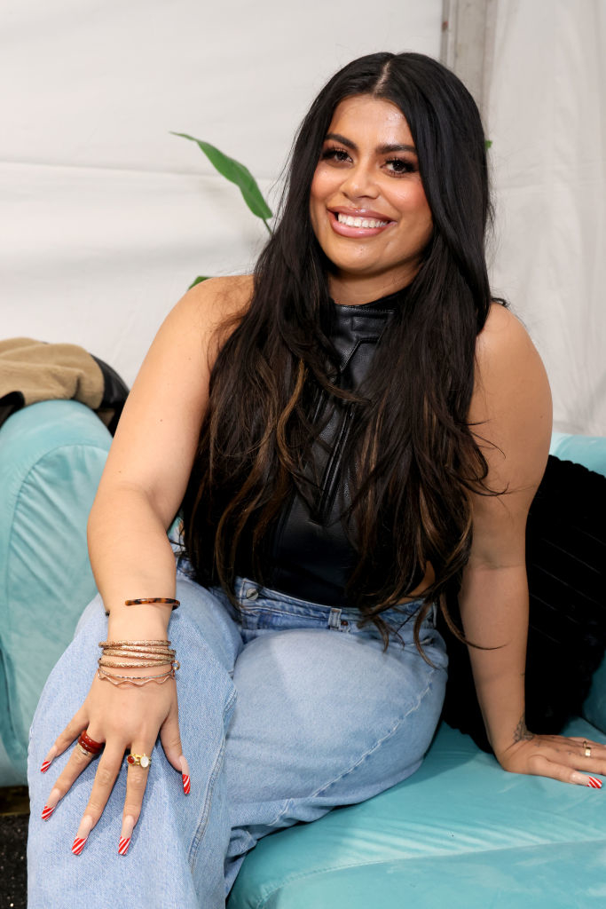 Woman seated on couch wearing a sleeveless black top and blue jeans, smiling at the camera