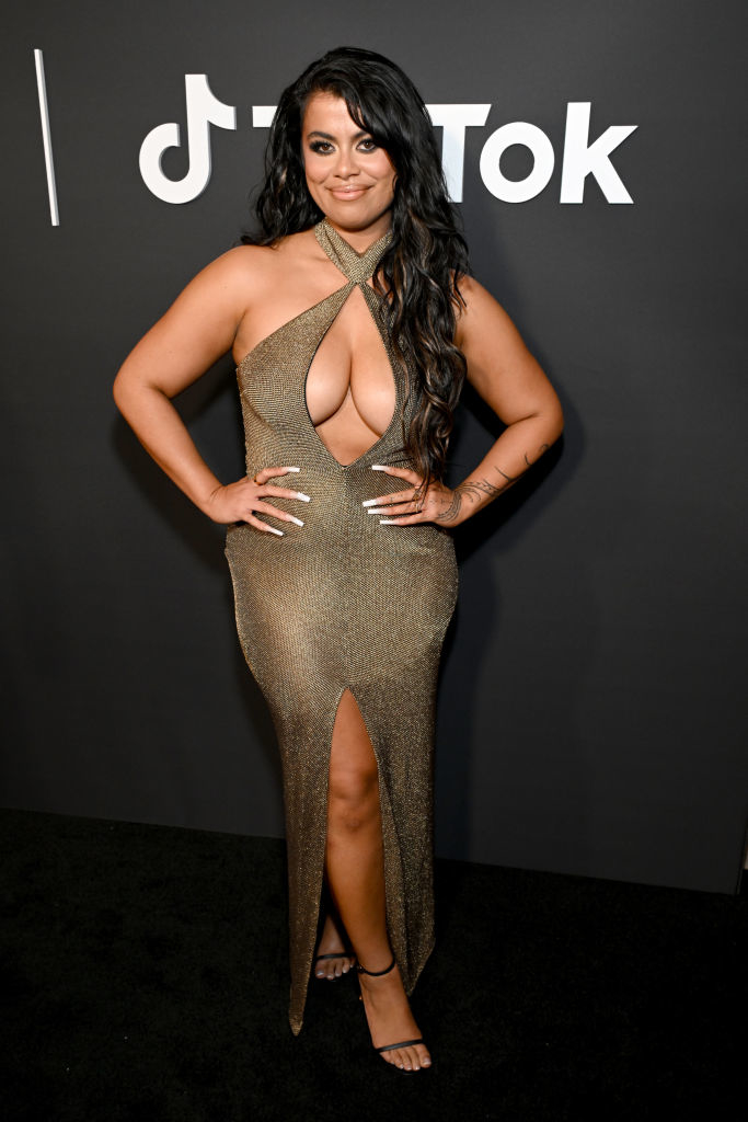 Woman in a glittering gown with a deep neckline and high slit, posing at an event