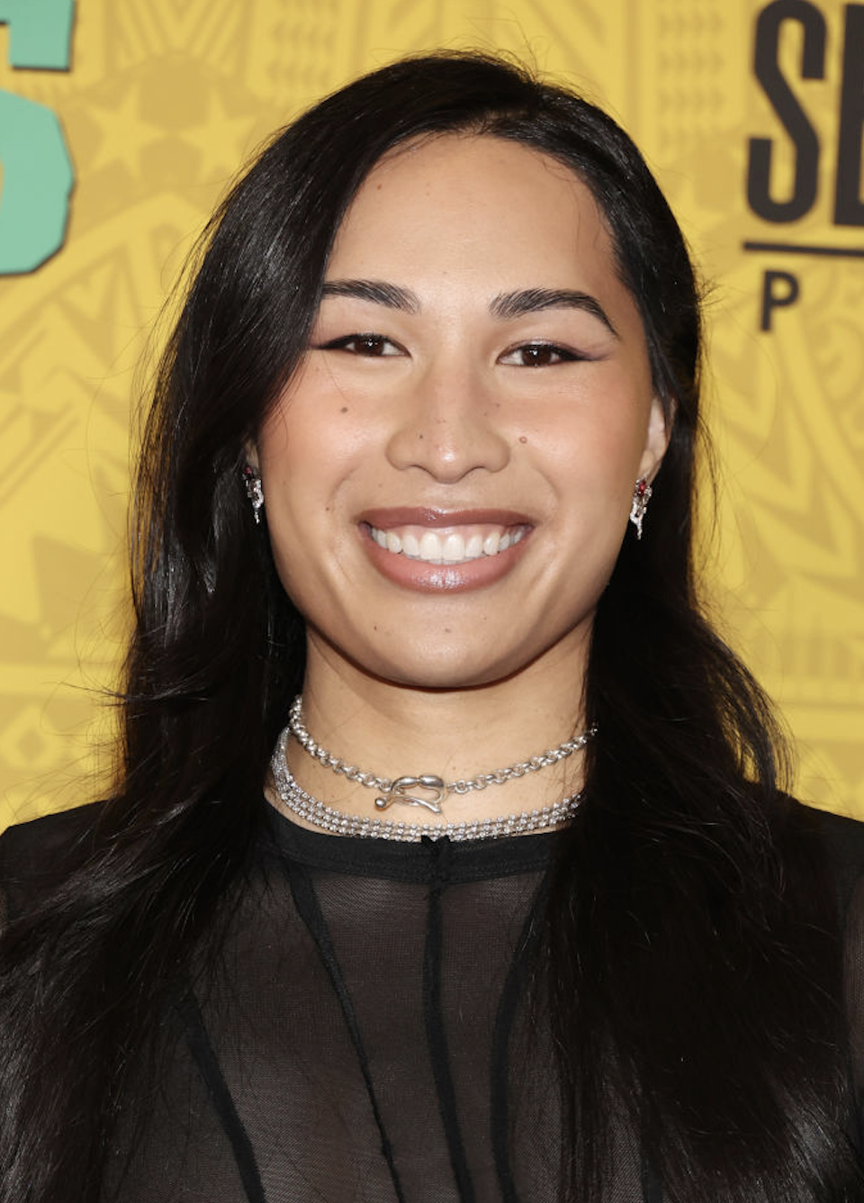 Woman in sheer top with layered necklaces smiling at an event