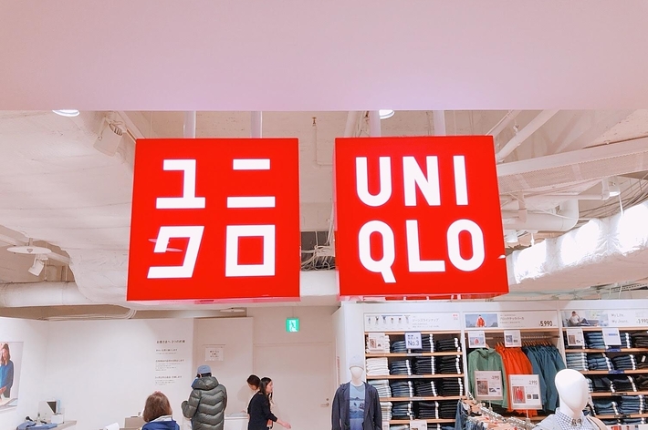 ユニクロの店内、ロゴとマネキン、買い物をする人たちが写っています。
