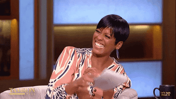 Talk show host sitting, laughing, and tossing papers in a striped top and large earrings