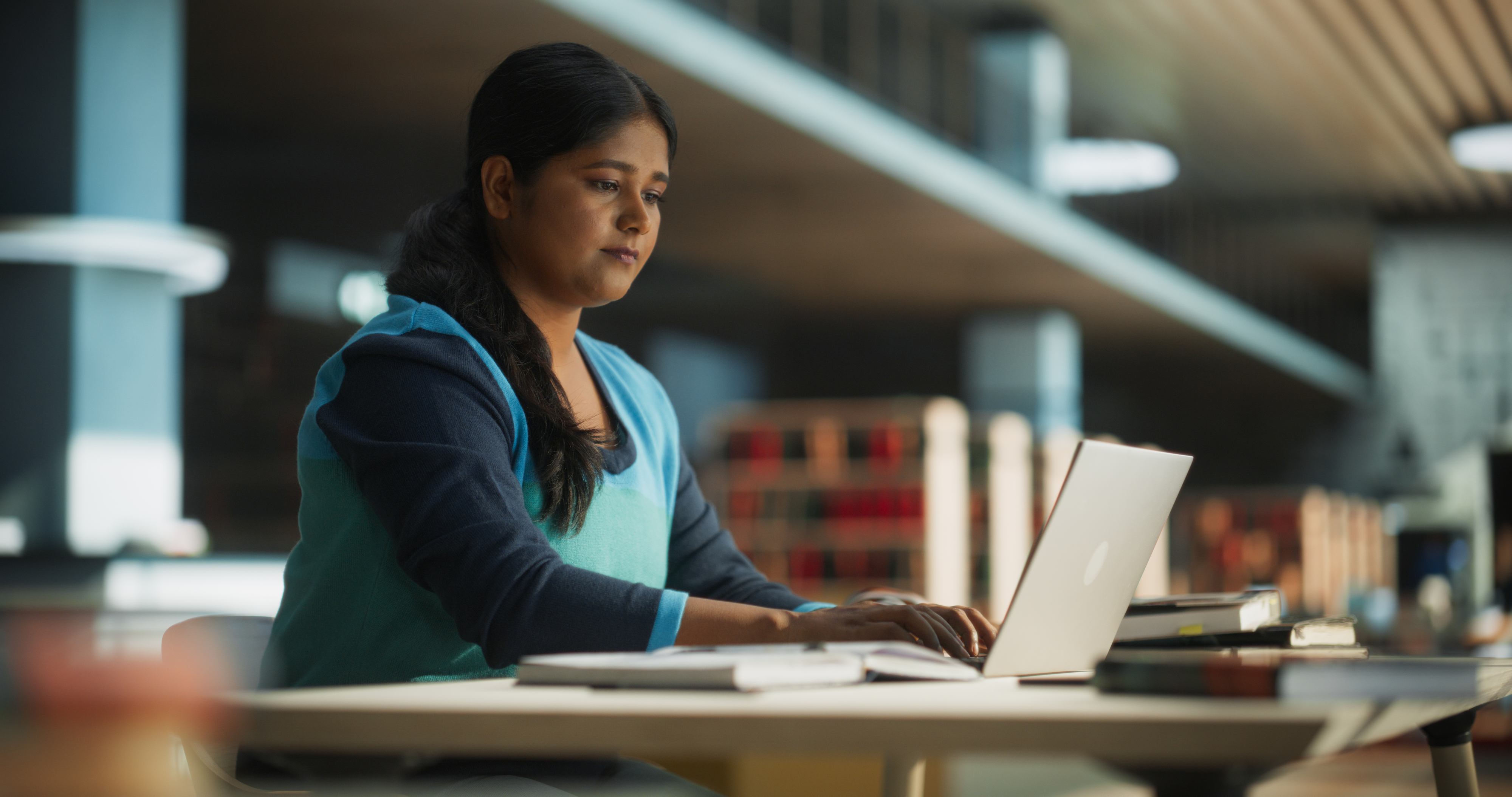 A woman focused on work at a laptop in a library setting