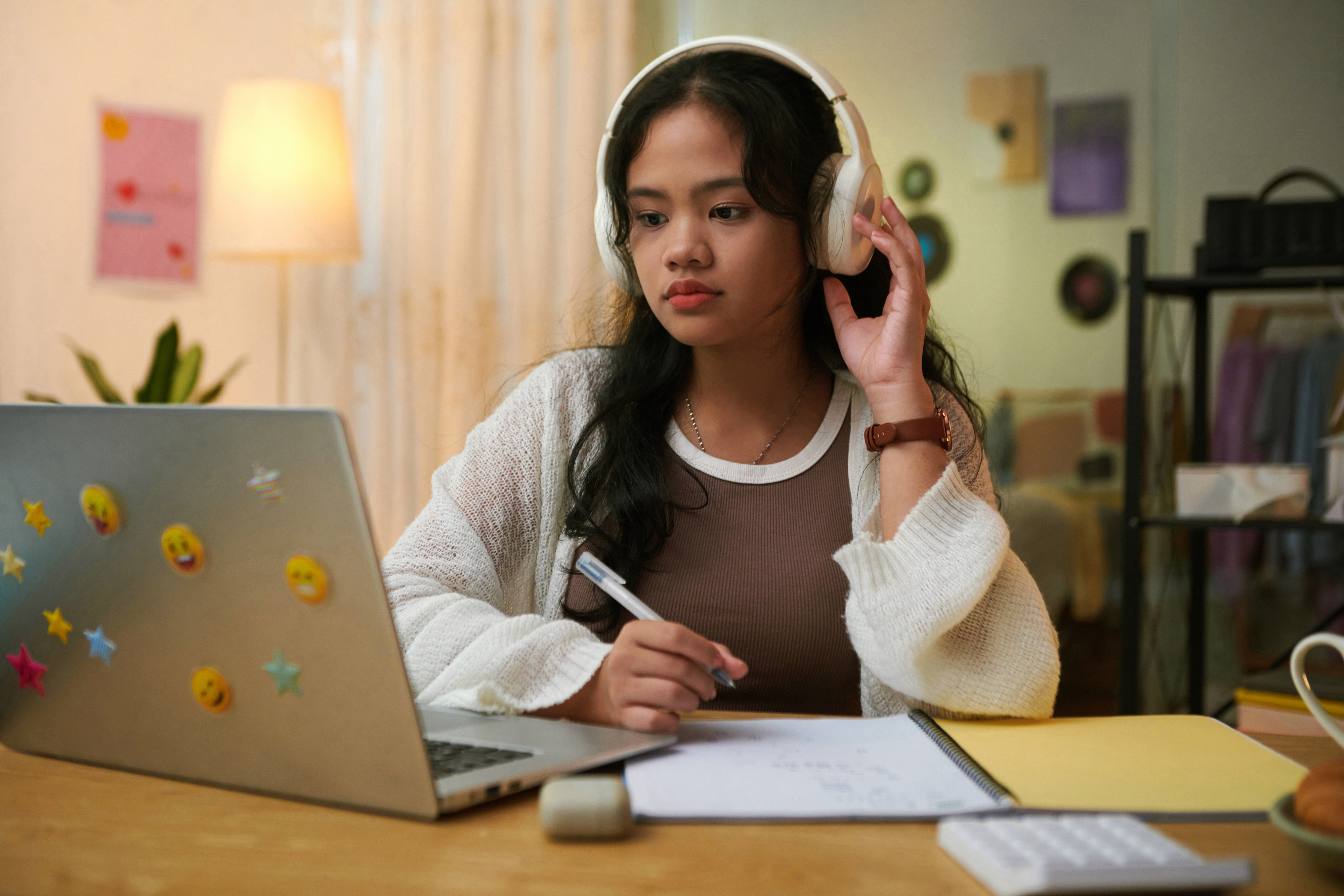 Young woman studying at a desk wearing headphones with a laptop and notes in front of her