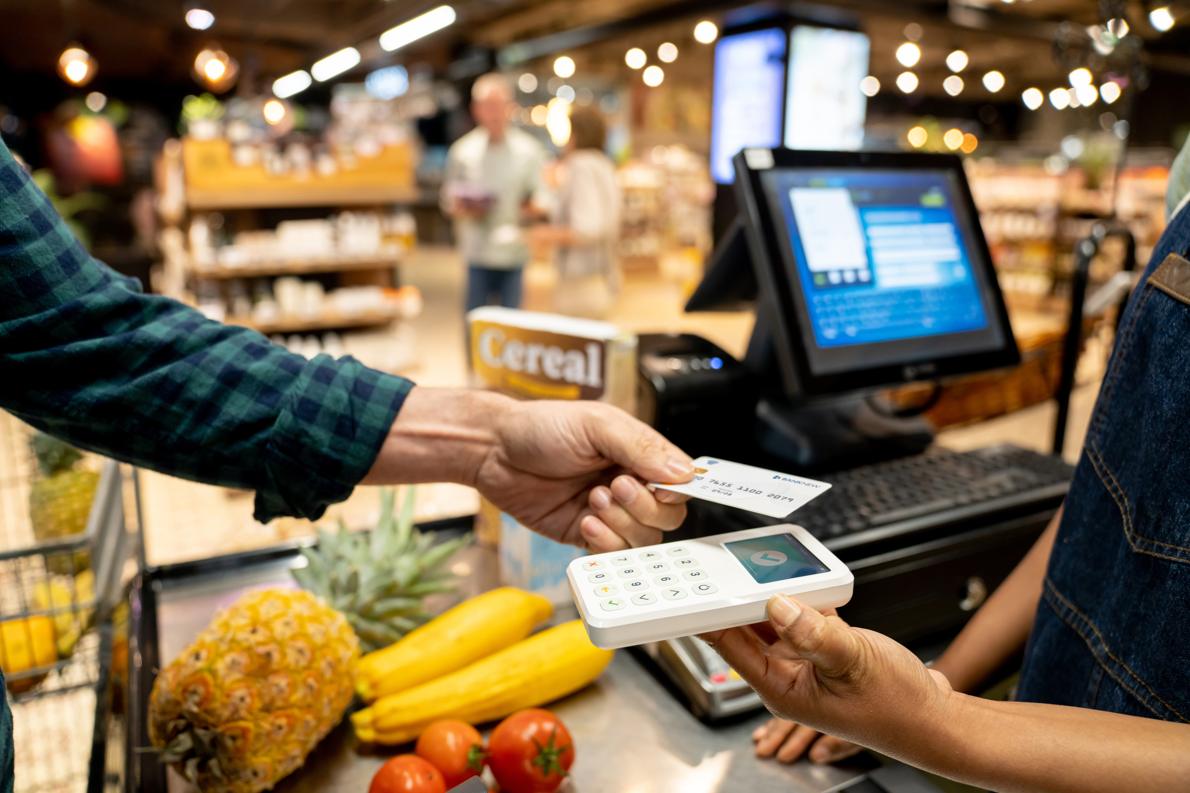 Person paying with a card at a grocery store checkout. Produce visible