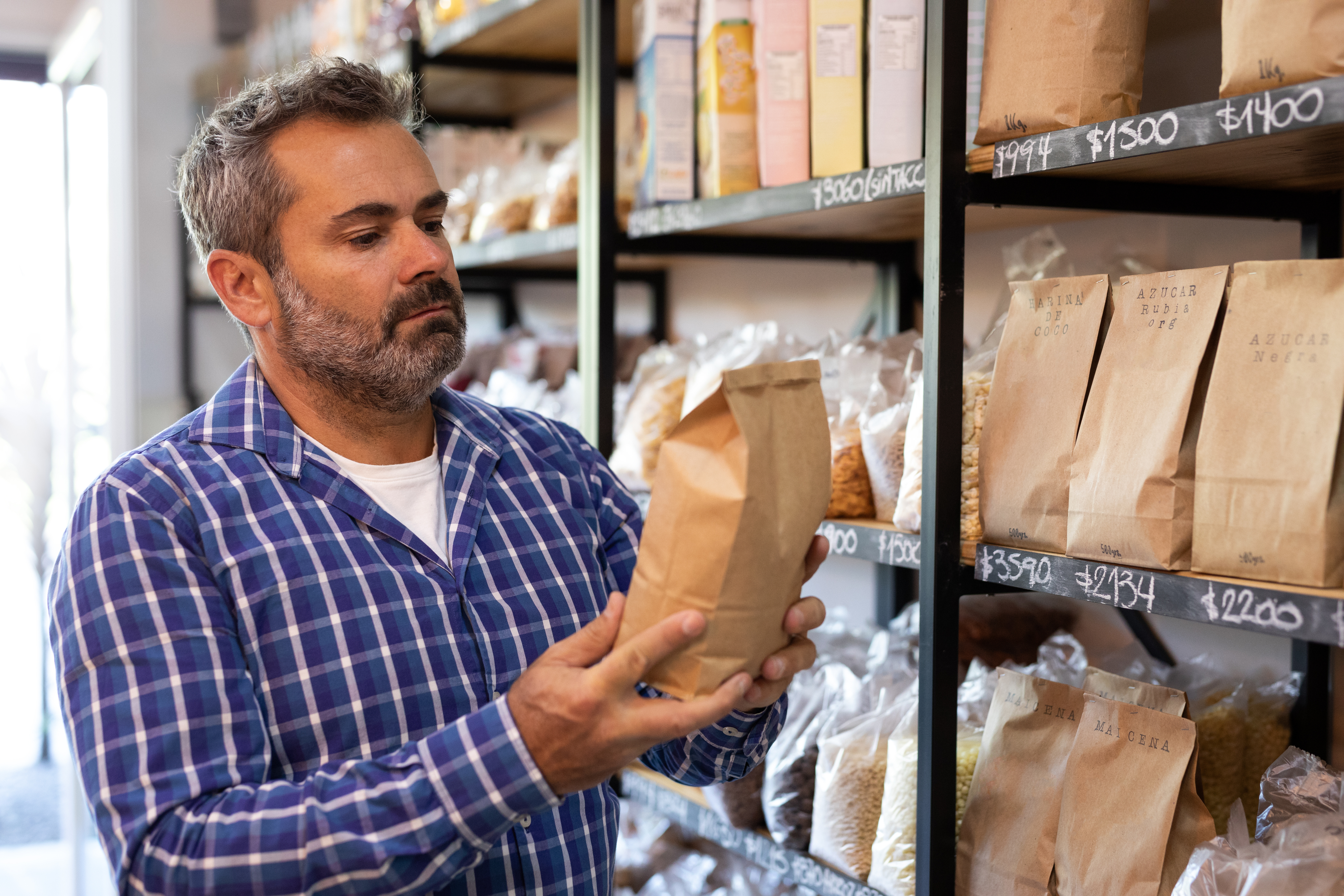 Man in a store examining a paper bag of food with shelves of products in the background