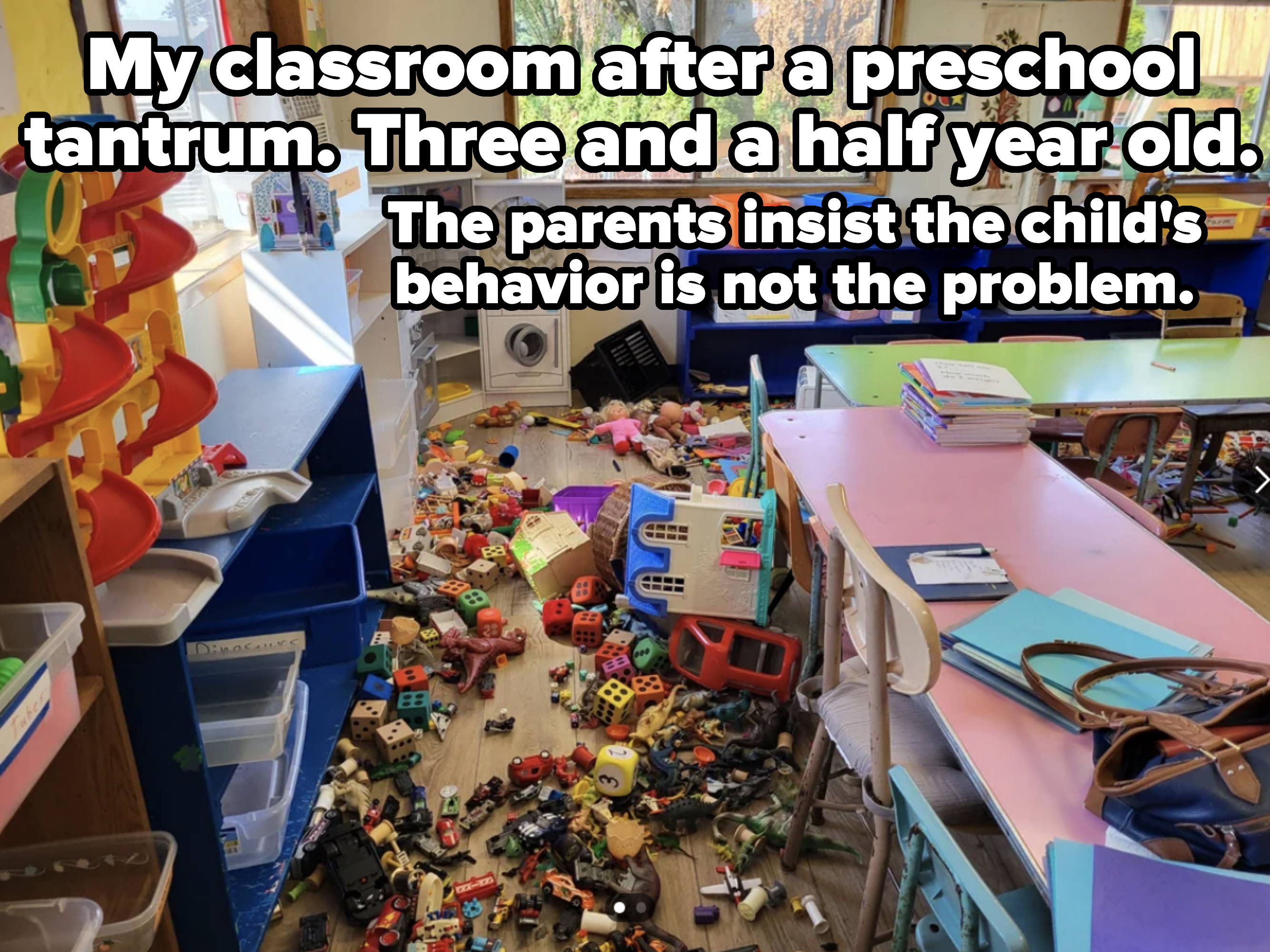 A cluttered classroom with toys, books, and furniture scattered across the floor and tables