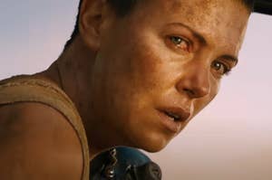 Close-up of a character, played by Charlize Theron, with an intense look and dirt on face