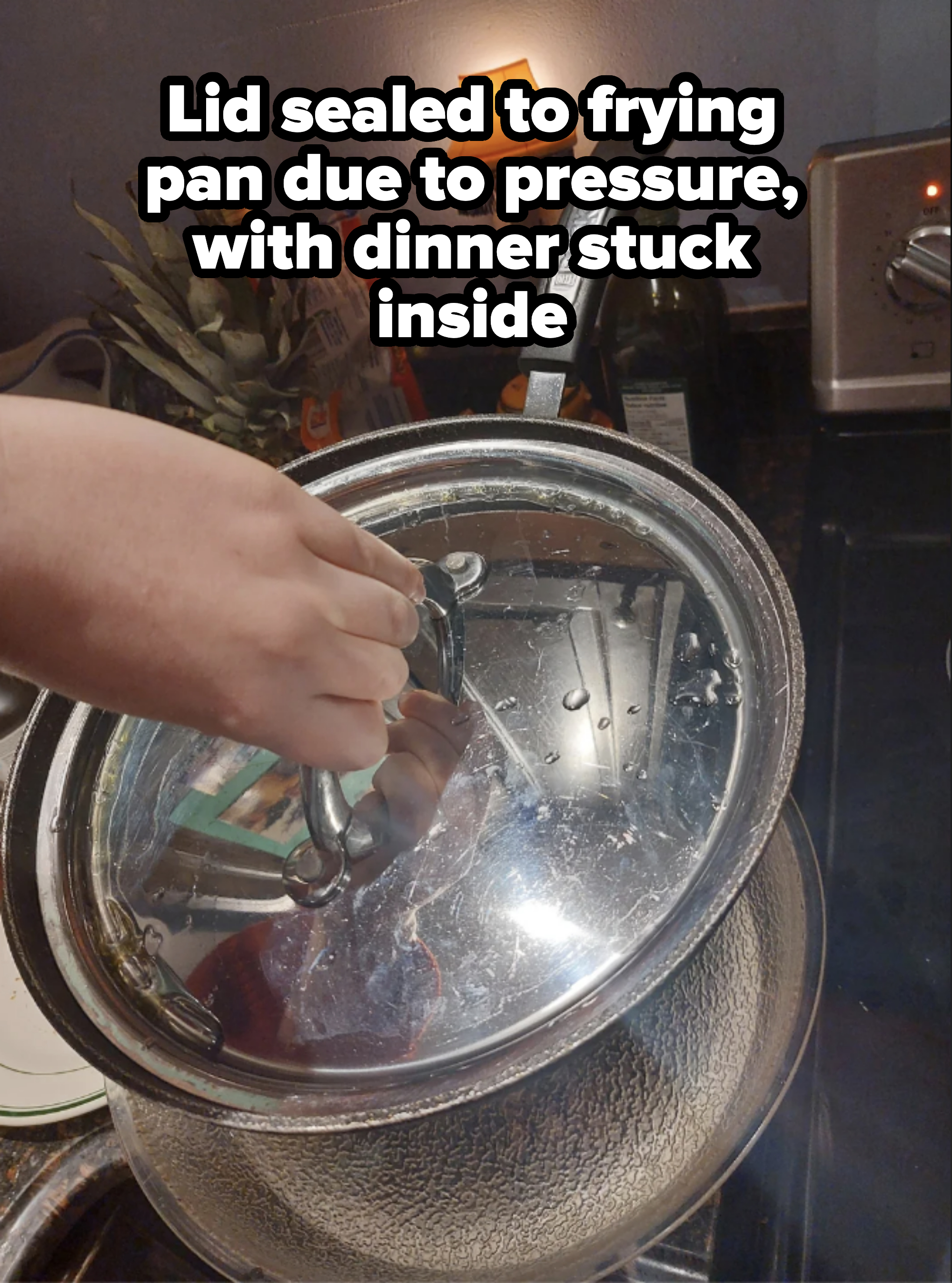 A person's hand holding a lid over a steaming pot on a kitchen stove with utensils and appliances in the background