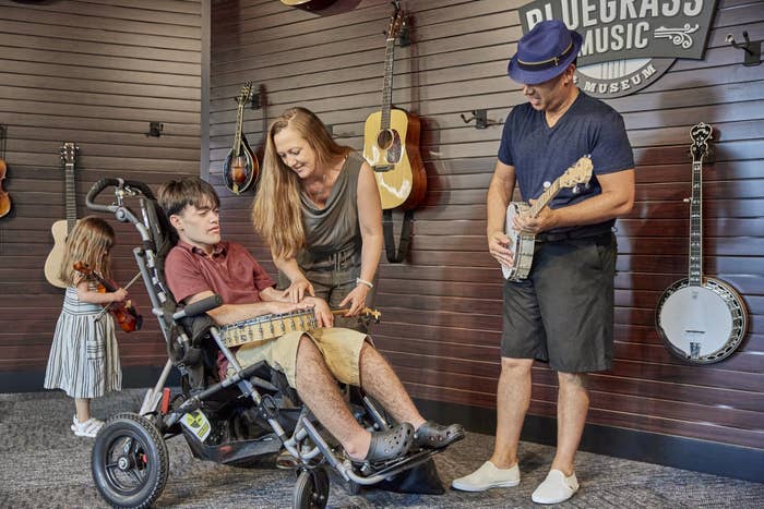 A family interacts with musical instruments at a Bluegrass music exhibit; a child in a wheelchair strums a guitar with assistance
