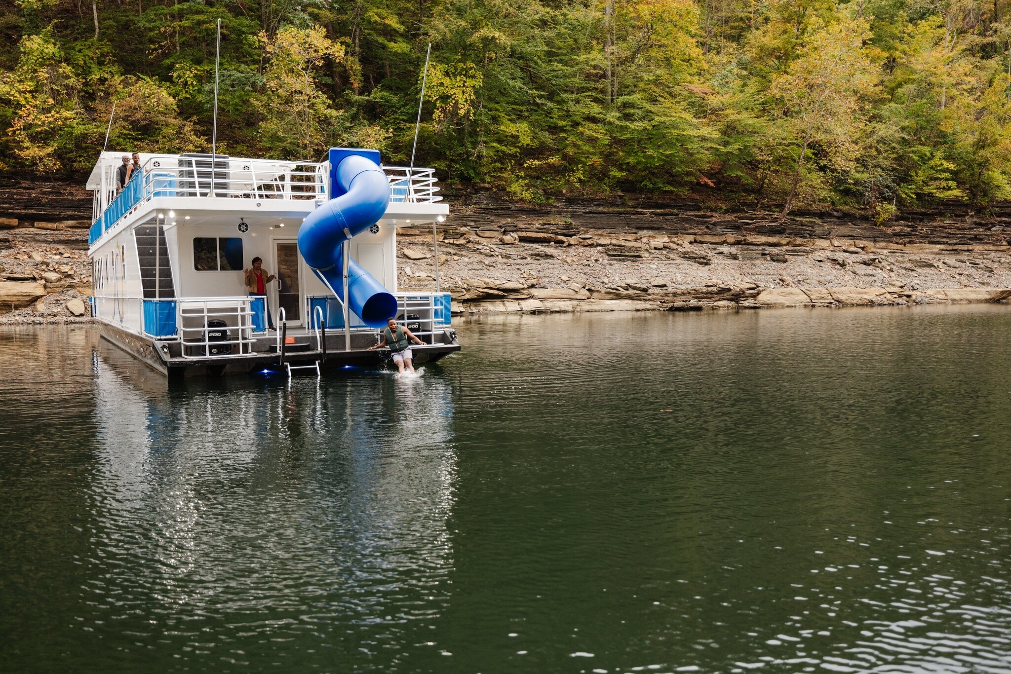 Houseboat with slide anchored near forested shoreline