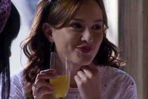 Blair Waldorf on "Gossip Girl" smiling slyly, holding a glass, wearing a white garment with a black headband