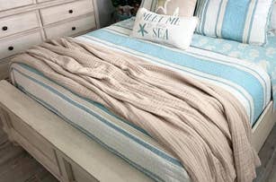 A neatly made bed with striped bedding and a decorative pillow with the text "Meet Me By The Sea."