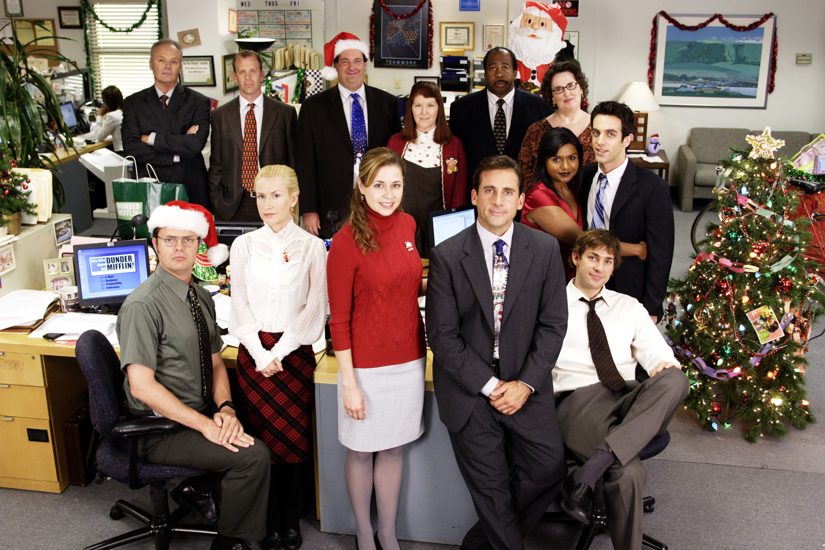 Office staff in festive attire pose for a holiday photo in a decorated workspace