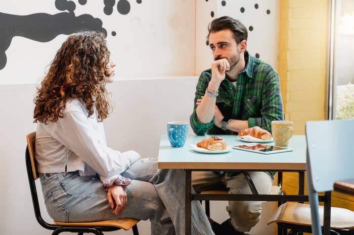 Two people seated at a cafe table engaged in conversation with drinks and pastries