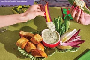 A selection of fresh vegetables and dip arranged on a table, hands dipping a carrot stick and holding a veggie bite