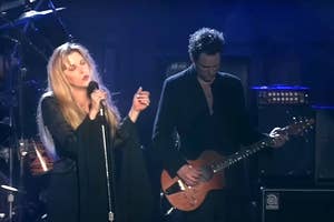 Stevie Nicks and guitarist perform on stage, with Nicks holding a microphone and Lindsey Buckingham focused on playing guitar