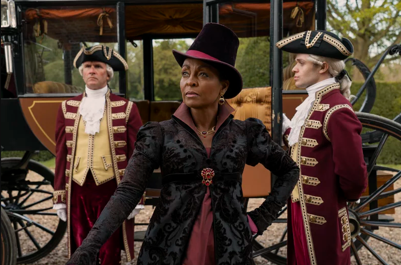 Personaje femenino vestido de época con sombrero, rodeado de personajes en trajes de carruaje. Escena de película o serie