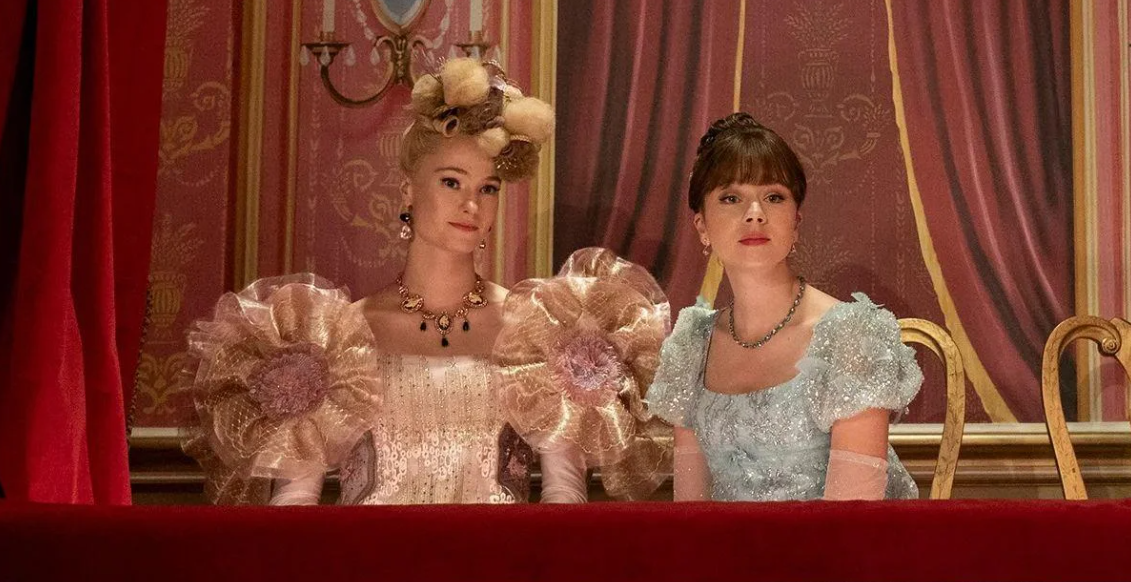 Dos personajes de la serie Bridgerton, con vestidos de época sentadas y mirando hacia adelante