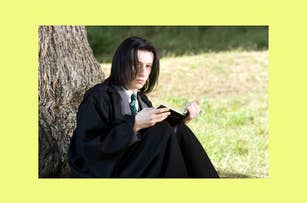 Young Snape in a black robe sits by a tree, focused on a book in their hands