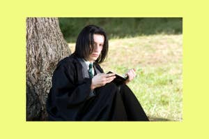 Young Snape in a black robe sits by a tree, focused on a book in their hands