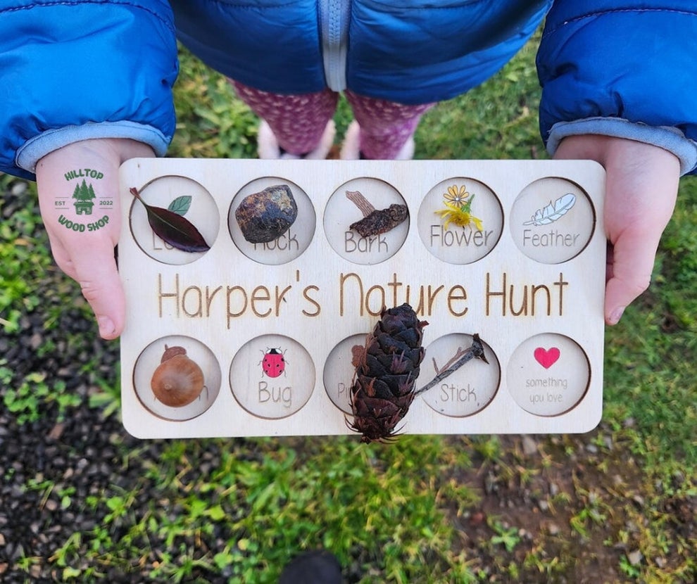 Child's hands holding a "Harper's Nature Hunt" board with slots filled with various natural items for an educational activity