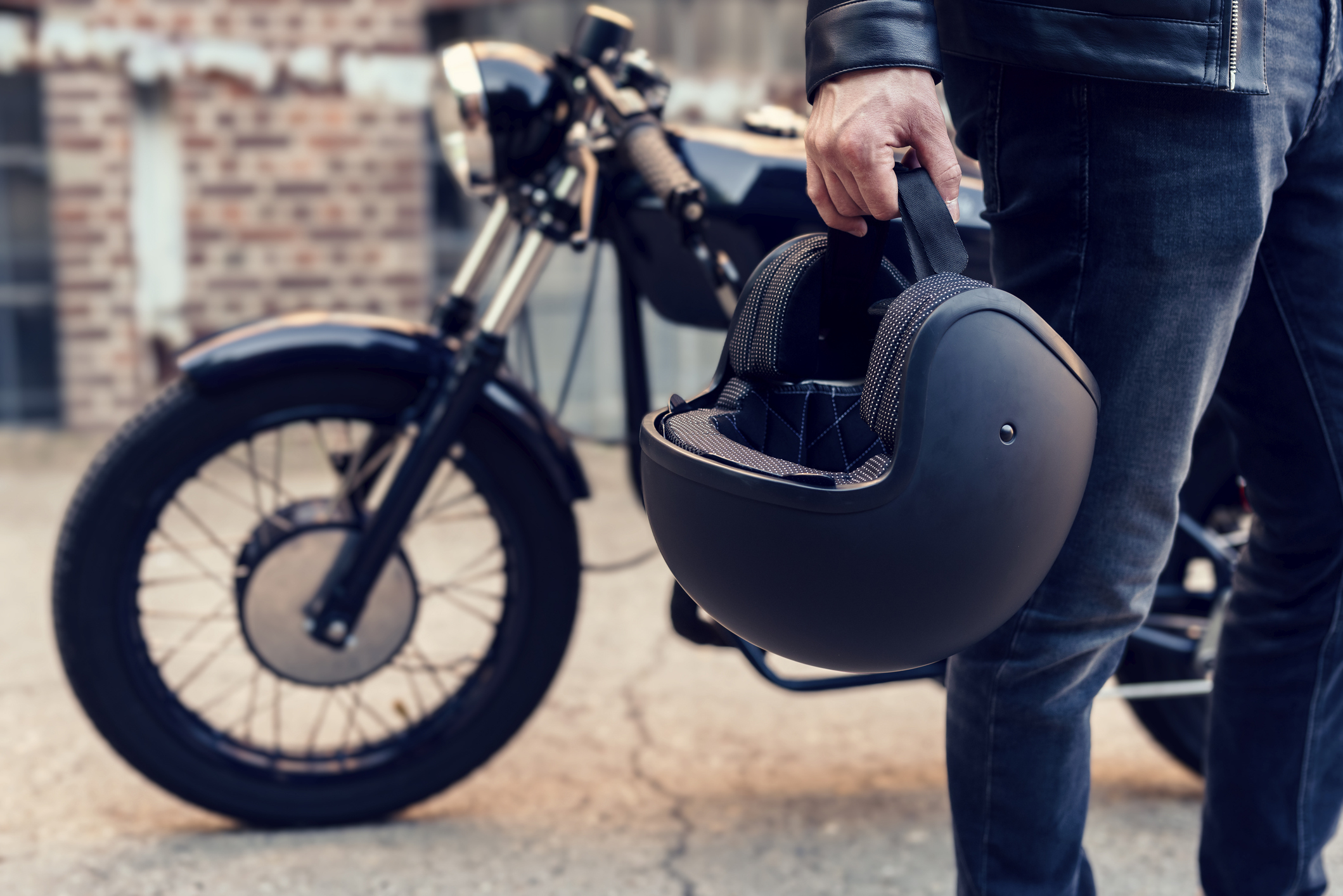Person holding a motorcycle helmet beside a parked motorcycle