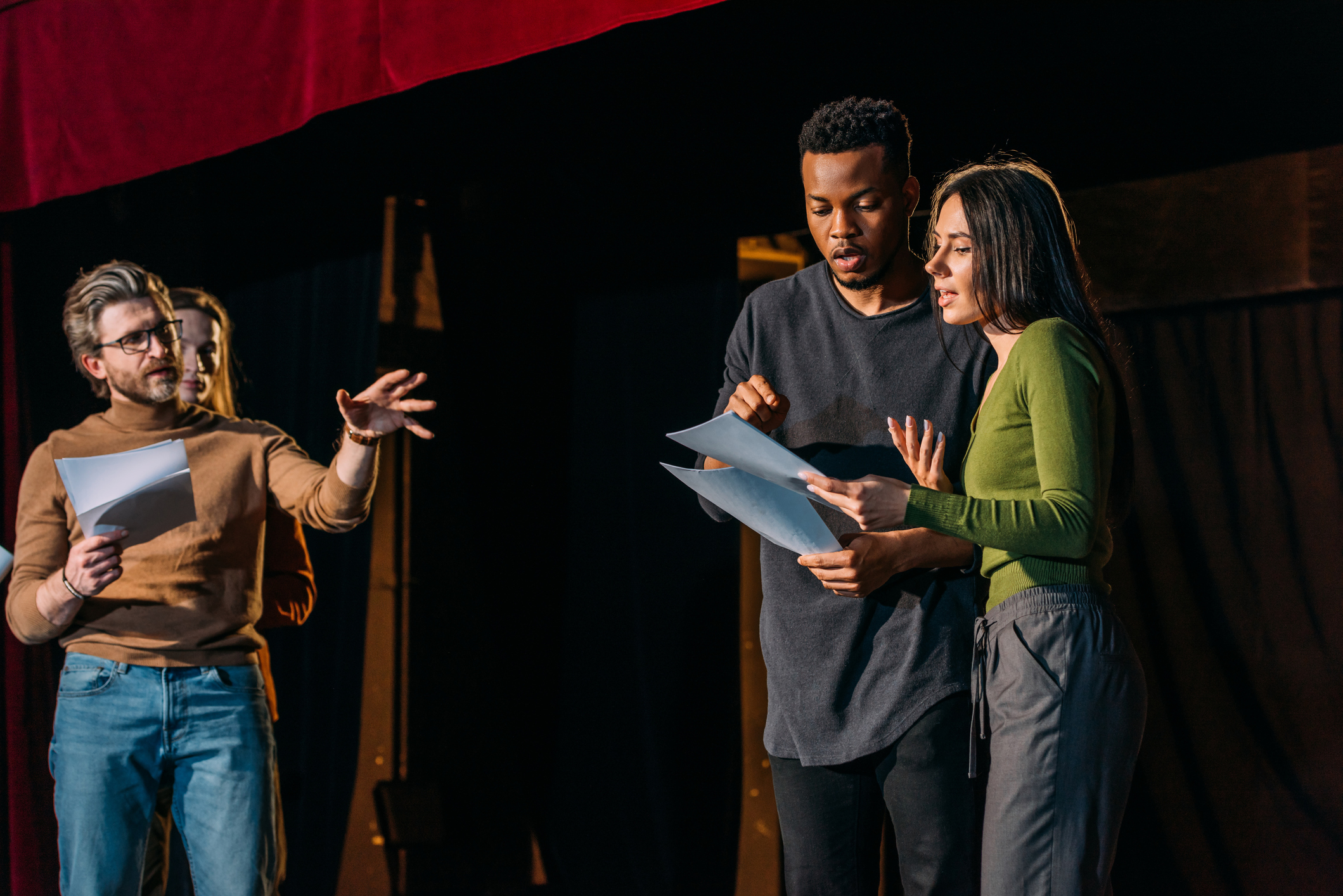 Three actors on stage rehearsing with scripts in hand, engaging in a dramatic scene