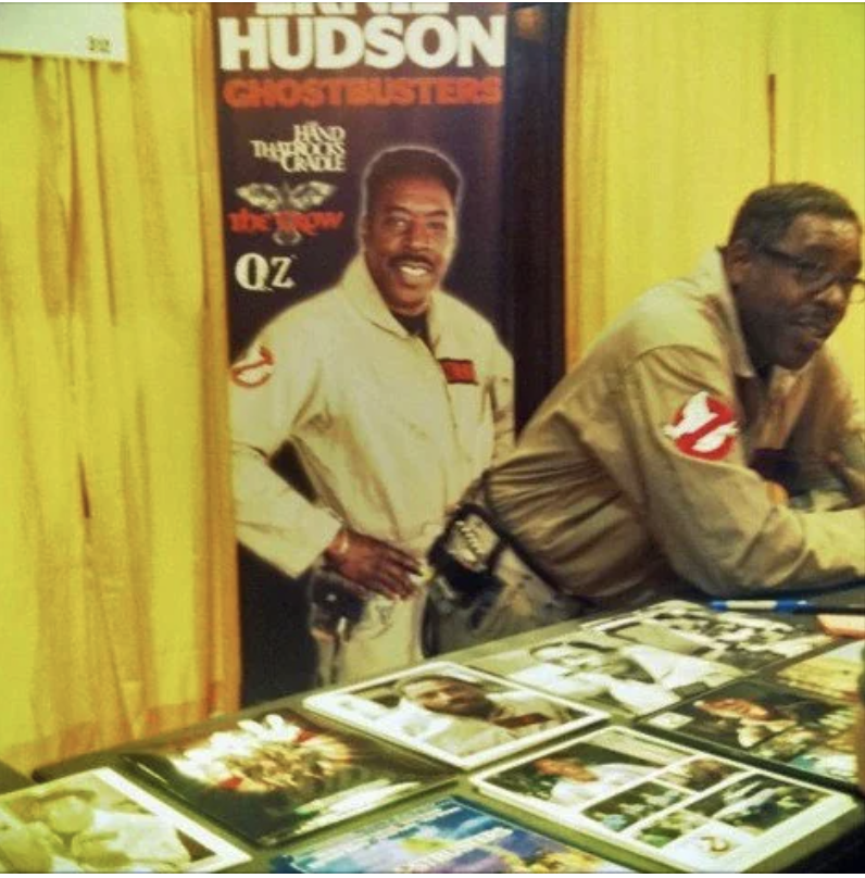 Actor Ernie Hudson at a convention table, with Ghostbusters memorabilia, including a movie poster