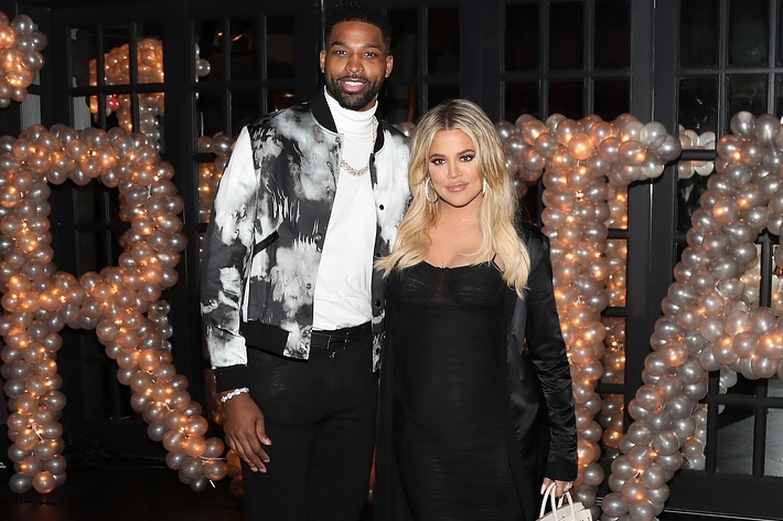 Tristan Thompson and Khloe Kardashian in formal wear, posing with a balloon arch backdrop