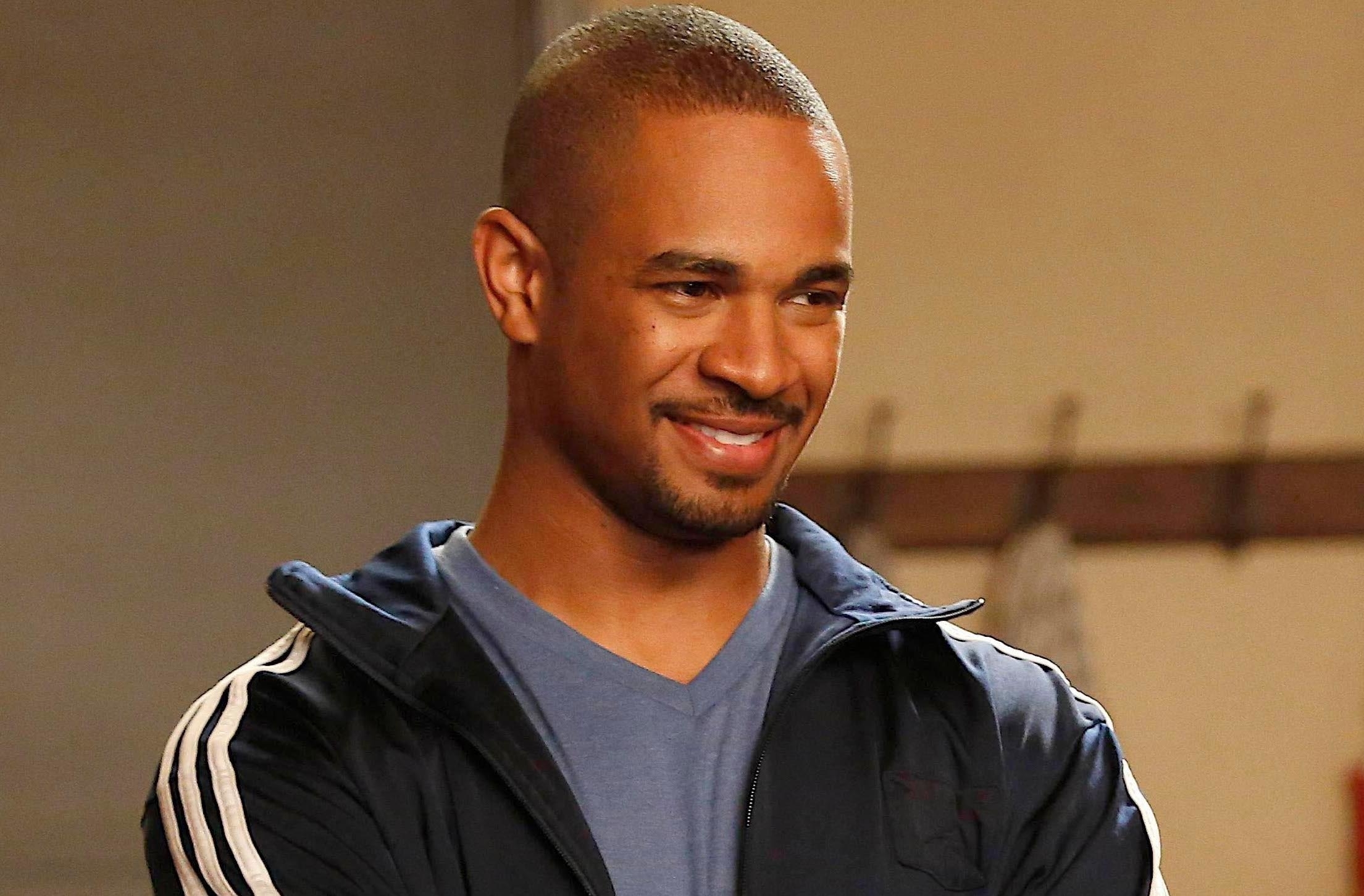Actor in a blue tracksuit smiling in a TV show scene