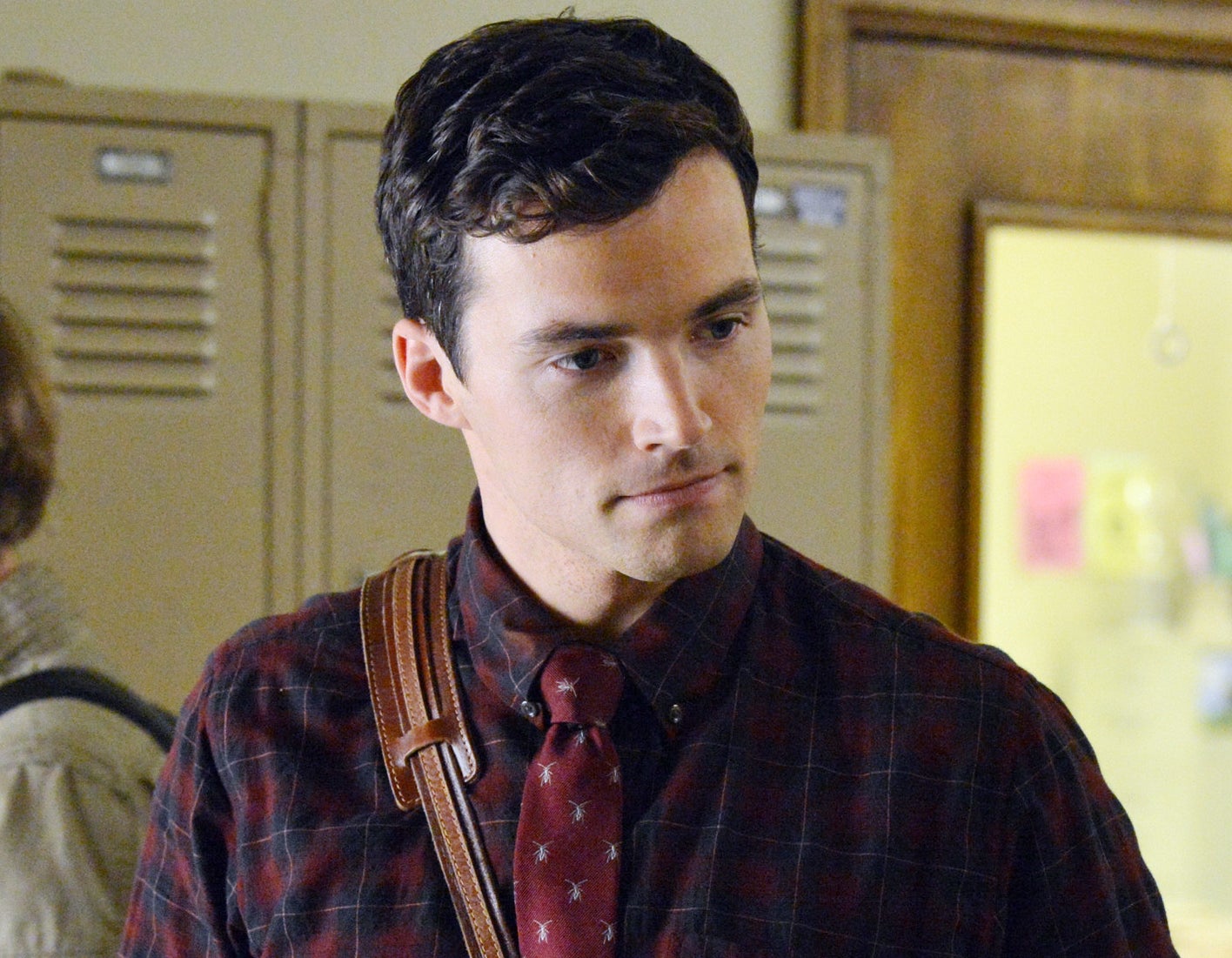 Actor in a plaid shirt and tie carrying a messenger bag talking to a female co-star in a denim jacket