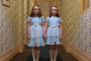 Twin girls in matching blue dresses stand in a hotel hallway, resembling the Grady twins from "The Shining"