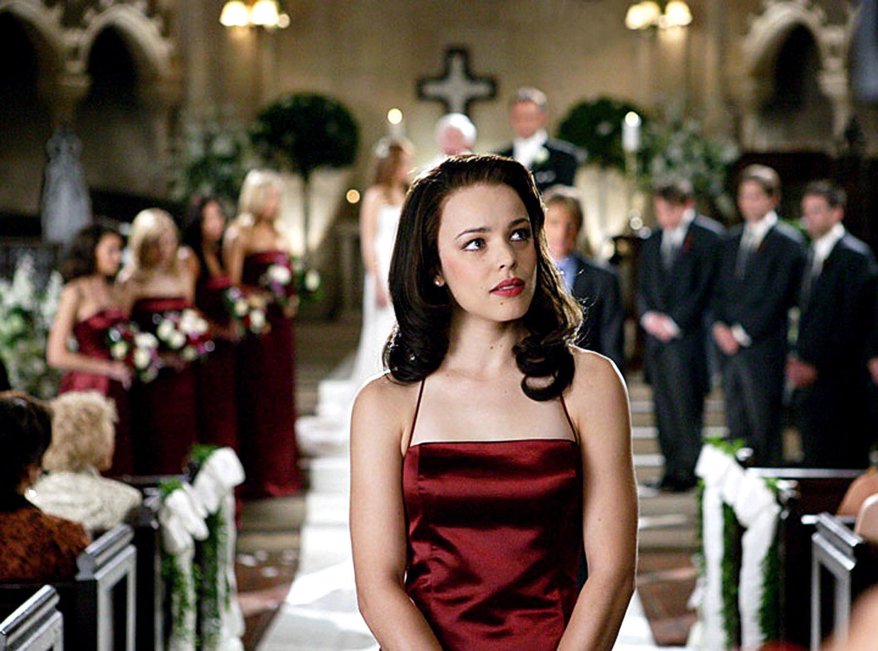 Rachel McAdams in a red bridesmaid dress pondering down a wedding aisle