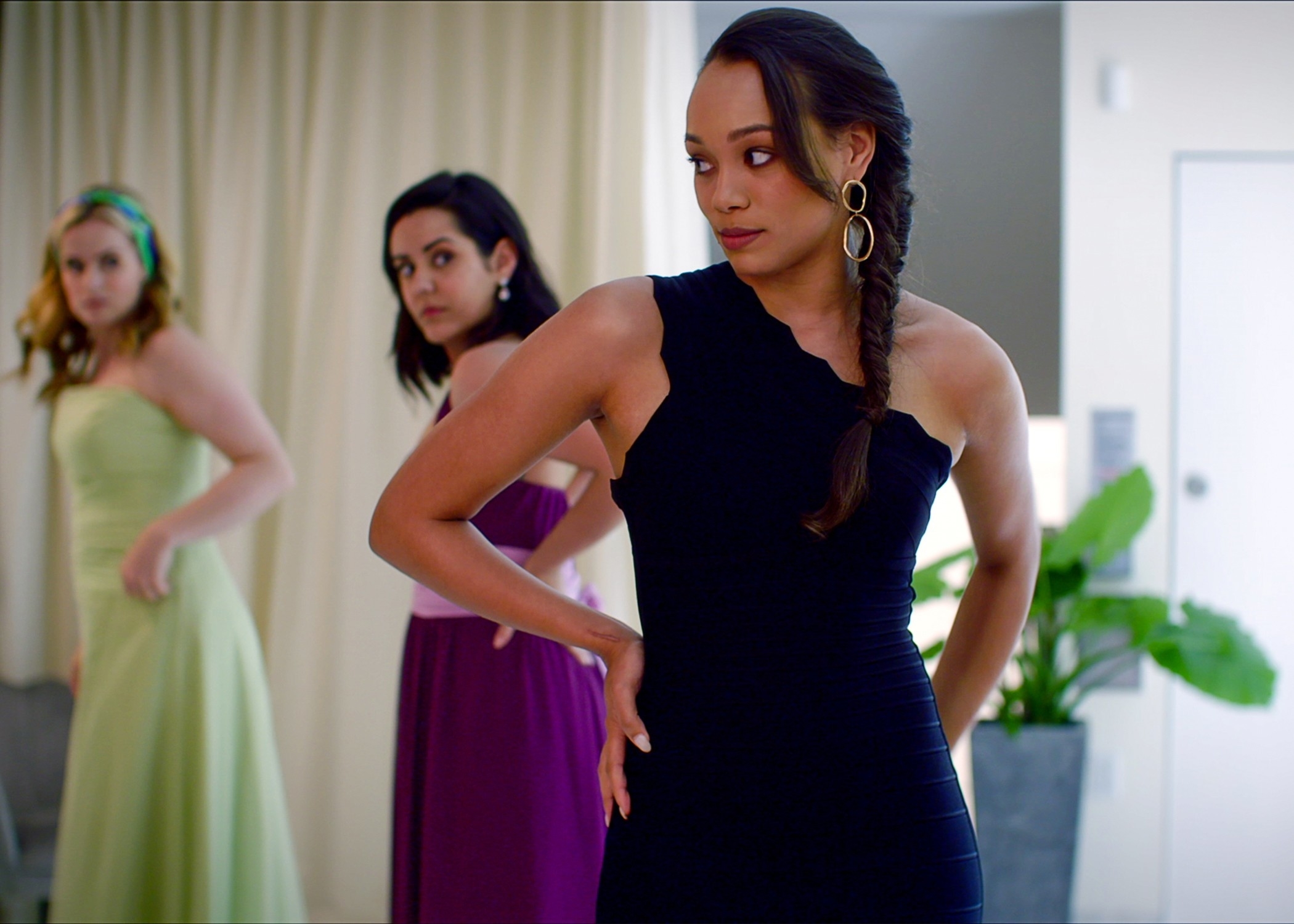 Three women in elegant dresses; one in black, others in green and purple, looking aside with serious expressions