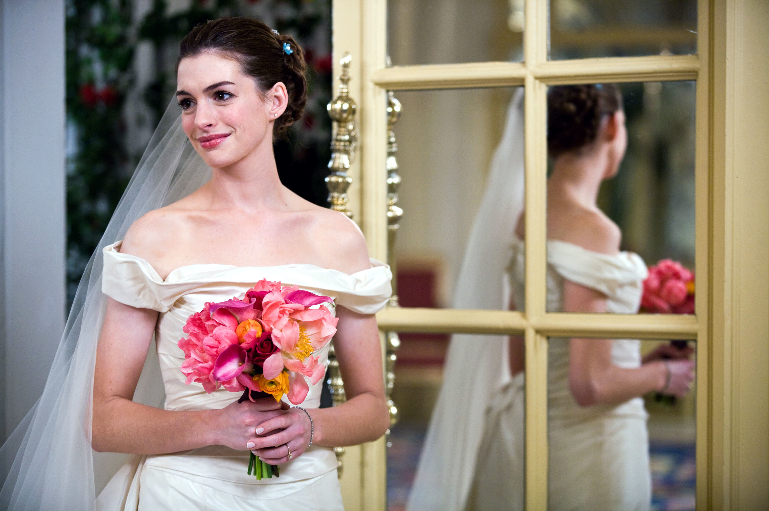 Anne Hathaway wearing a shoulderless bridal gown and veil holding a bouquet of flowers