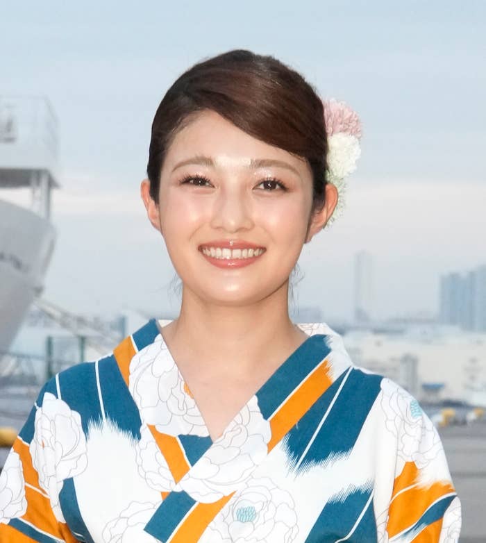 写真の女性は花柄の着物を着て、笑顔でカメラを見ています。