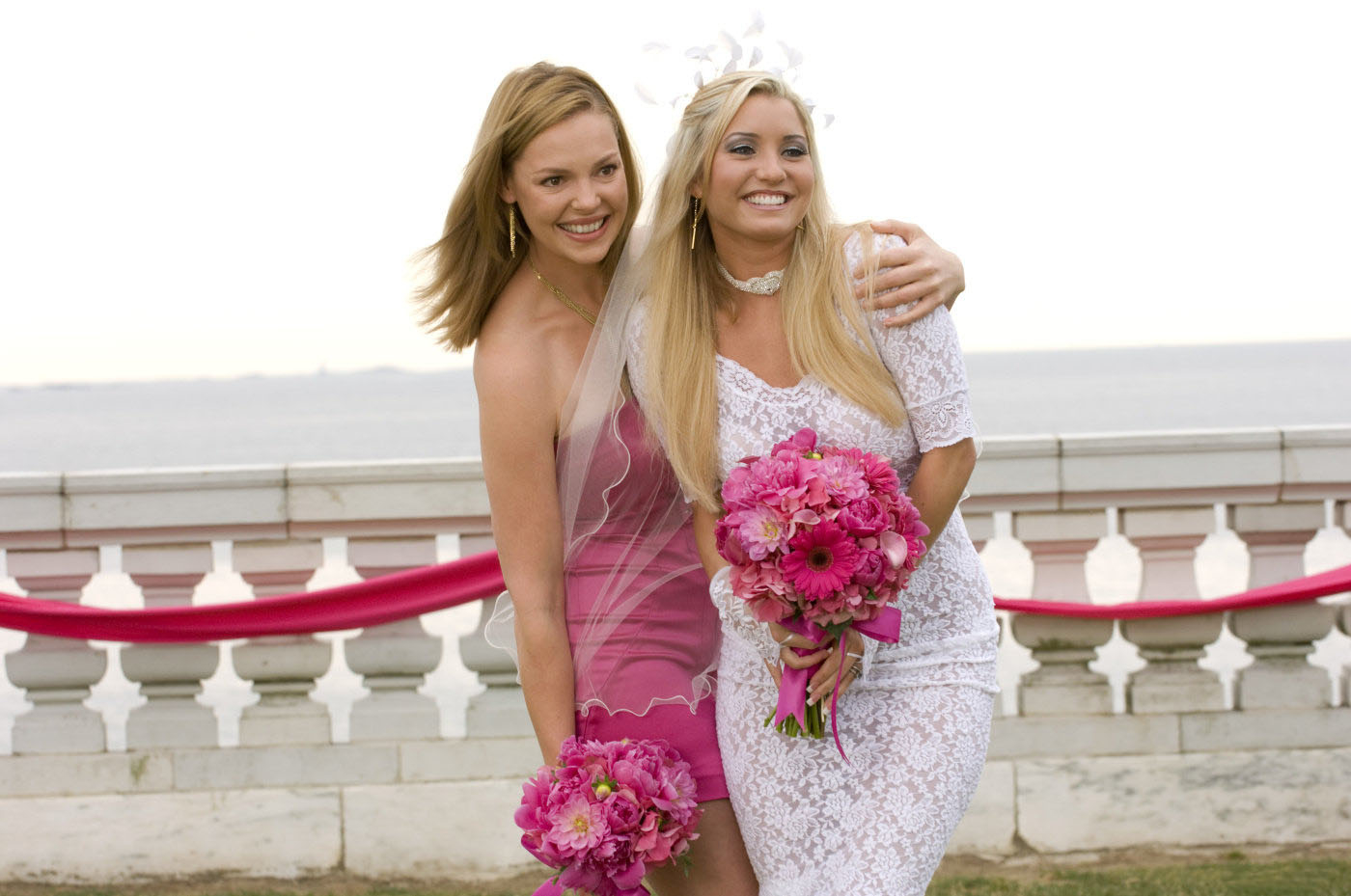 Katherine Heigel wearing a pink bridesmaids dress and holding a pink bouquet by a bride smiling