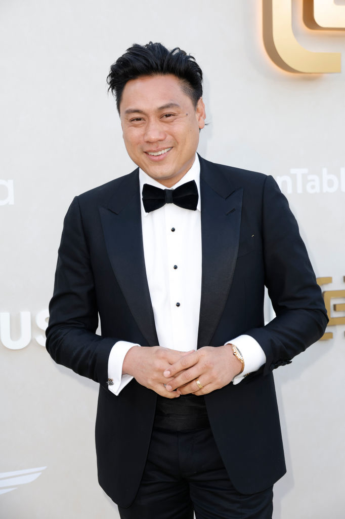 Man in a classic tuxedo with bow tie, smiling at camera, hands gently clasped