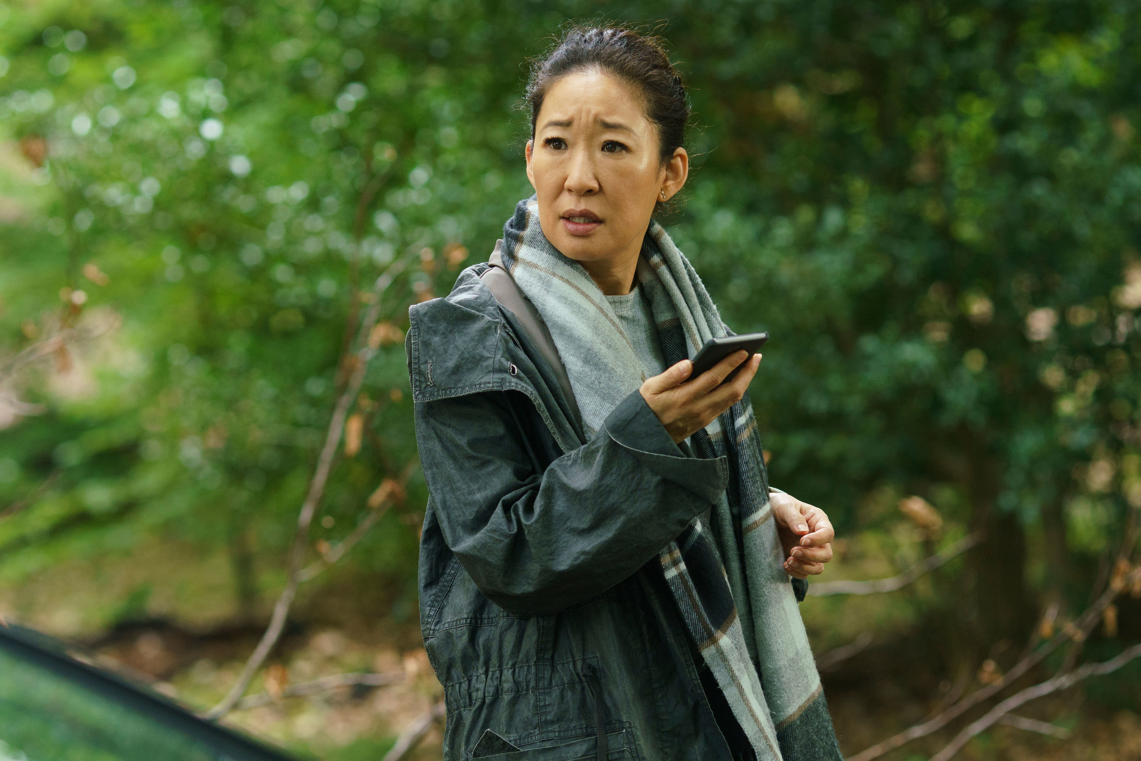 in a scene, Eve in a jacket holding a phone with a concerned expression in a wooded area