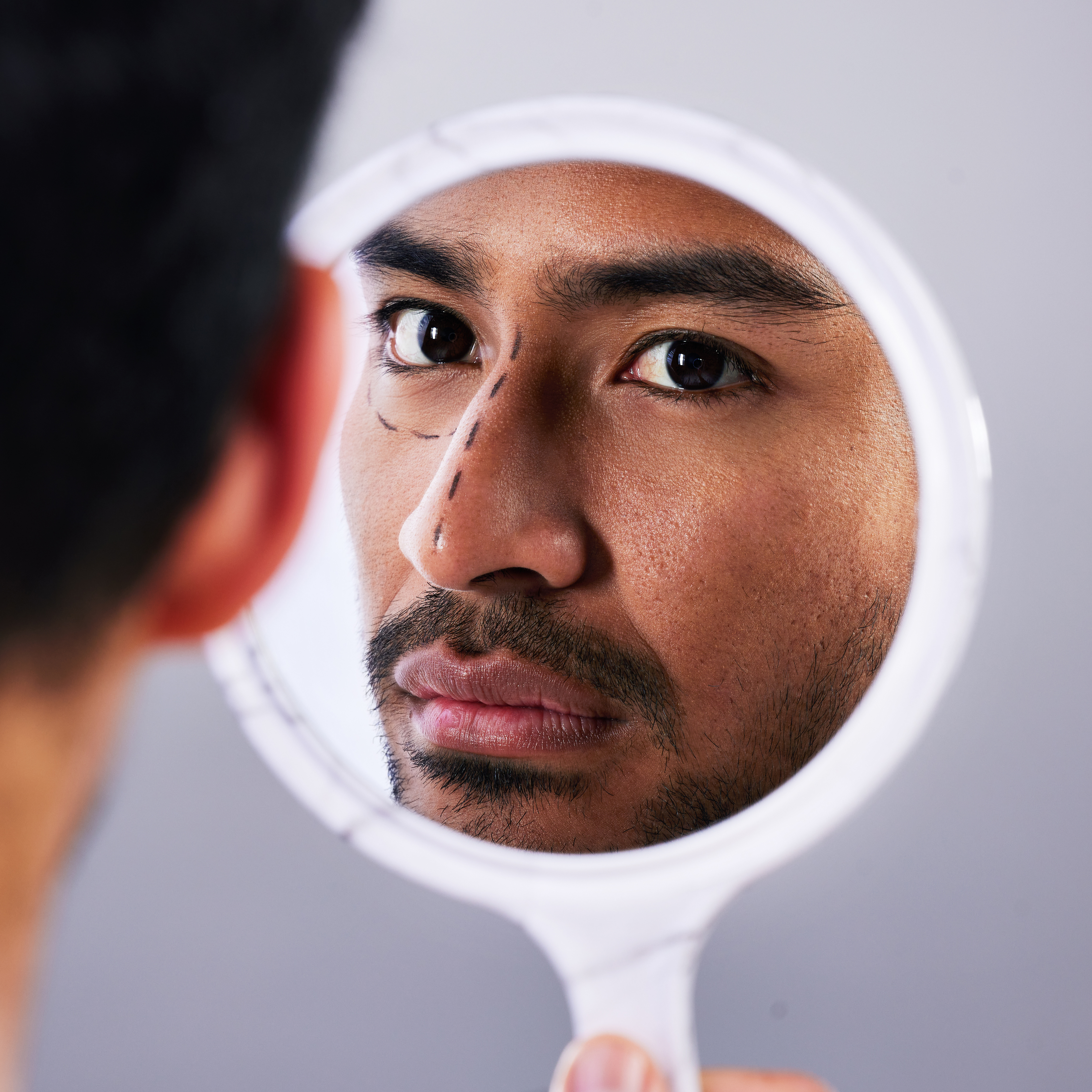 Person examining their reflection in a hand-held mirror focusing on their facial features