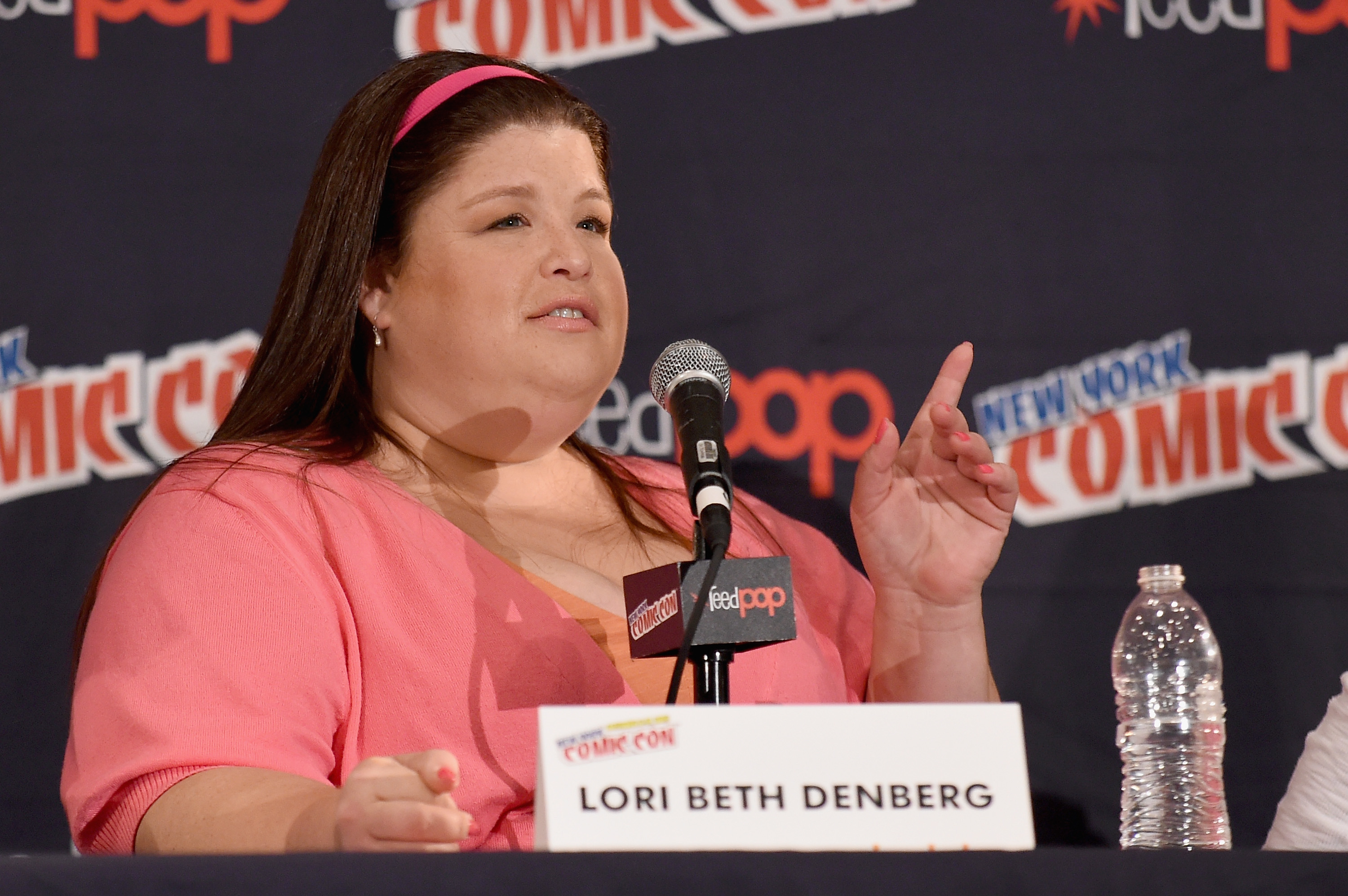 Lori Beth Denberg speaking at a panel with a microphone and a nameplate in front of her